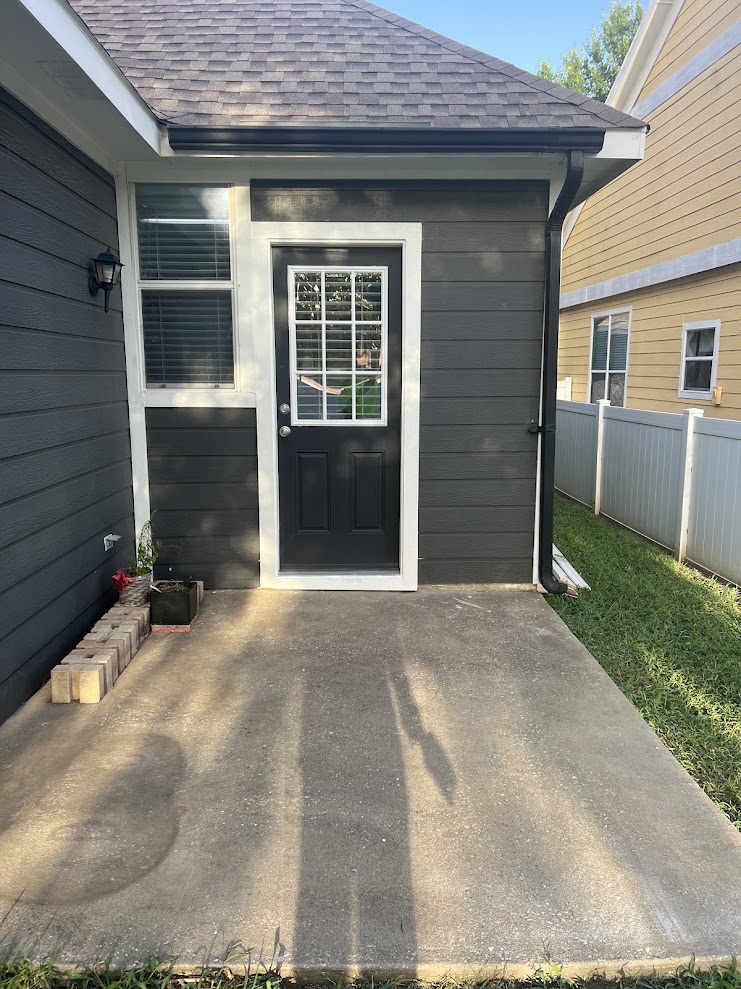 Completed exterior paint job by N&M Services showing the repainted siding, white trim and back entry door with its concrete patio.